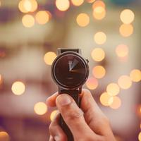 A person holding up a watch - pretty lights in background